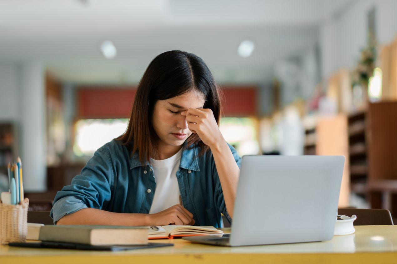 Studentin sitzt gestresst vor Laptop und lernt Strategien, um beim Bachelorarbeiten schreiben lassen Ruhe zu bewahren