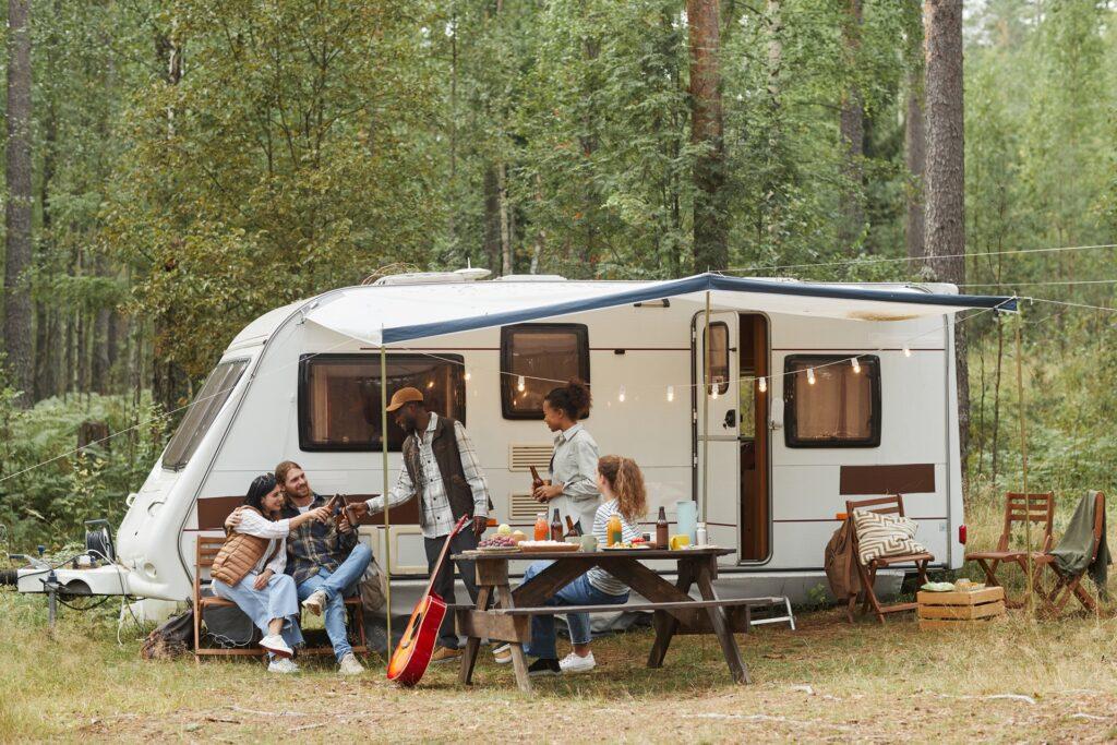 Gruppe von Freunden beim Campen vor Wohnwagen im Wald | Petroleum Heizung Camping