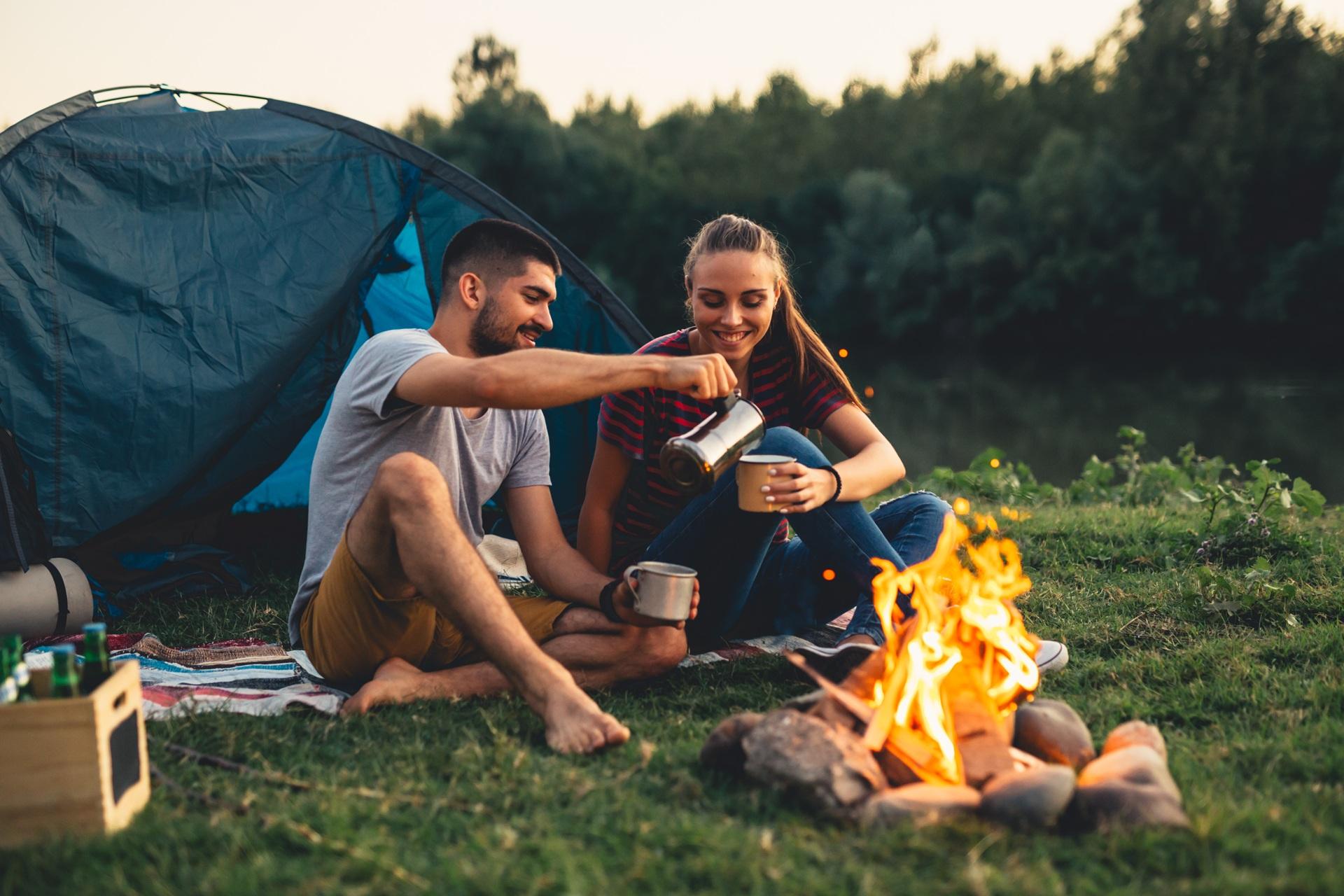 Paar sitzt am Feuer und trinkt Kaffee beim Zelten | Petroleum Heizung Camping